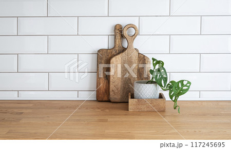 Cozy white kitchen with wooden countertop, flowers and cutting boards in a minimalist interior  117245695