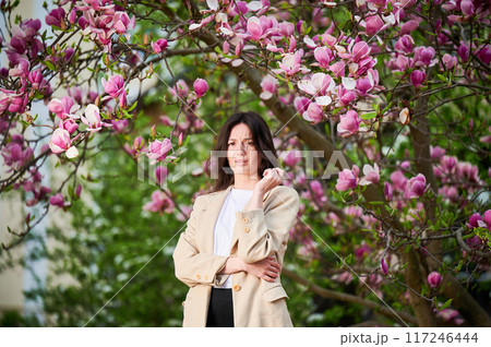 Woman allergic suffering from seasonal allergy at spring in blossoming garden at springtime. Young woman sneezing, having runny nose in front of blooming tree. Spring allergy concept 117246444