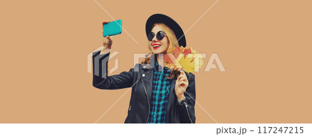 Autumn portrait of stylish happy smiling young woman taking selfie with phone holding yellow leaves Autumn portrait of stylish happy smiling young woman taking selfie with phone holding yellow leaves 117247215
