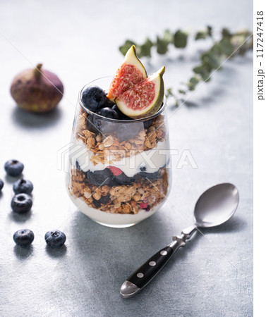 Delicious natural yogurt with granola and berries in a glass on a blue background. Delicious natural yogurt with granola and berries in a glass on a blue background. 117247418