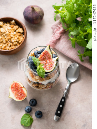 Delicious natural yogurt with muesli, figs and berries in a glass on a pink background with mint. Delicious natural yogurt with muesli, figs and berries in a glass on a pink background with mint. 117247426