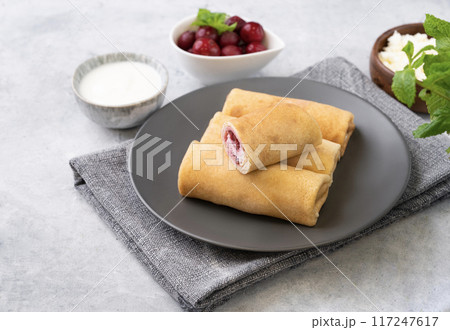 Homemade crepes with chery berry and a cottage cheese on a plate on a blue background 117247617