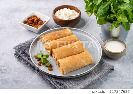 Homemade crepes with cottage cheese and raisin on a plate on a blue background with sour cream 117247627