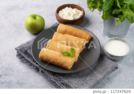 Homemade crepes roll with cottage cheese and apple on a plate on a blue background with sour cream  117247629