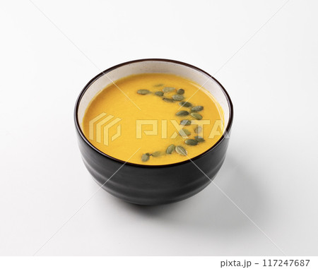 Autumn vegetarian pumpkin soup with cream and seeds on wooden plate on white isolated background. Autumn vegetarian pumpkin soup with cream and seeds on wooden plate on white isolated background. 117247687