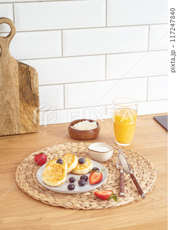 Cheesecakes or cottage cheese with fresh berries, sour cream and orange juice on a kitchen table. 117247840