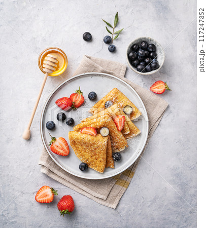 Homemade thin pancakes or crepes with fresh blueberries and strawberries and honey on a plate  117247852