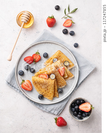 Flat lay homemade thin pancakes or crepes with fresh blueberries and strawberries and honey Flat lay homemade thin pancakes or crepes with fresh blueberries and strawberries and honey 117247855