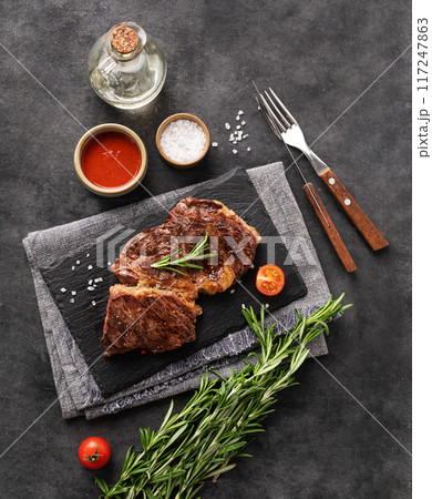 BBQ  beef steak grill with sauce, oil, salt and rosemary on black slate on dark  background. 117247863