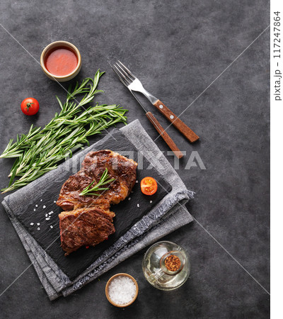 BBQ  beef steak grill with sauce,tomatoes and rosemary on black slate on dark  background. 117247864