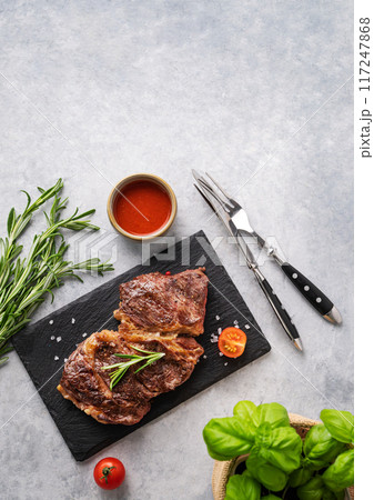 BBQ grilled beef steak with sauce, rosemary and basil on black slate on light  background. 117247868