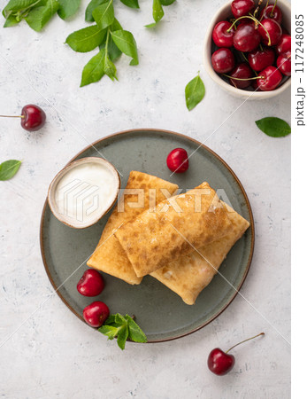 Delicious homemade pancakes or crepes  with fresh cherries and sour cream on a dark plate  117248085