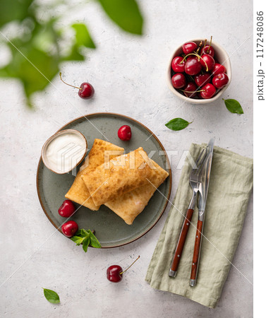 Delicious homemade pancakes or crepes  with fresh cherries and sour cream on a dark plate 117248086