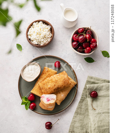 Flat lay homemade pancakes or crepes with cottage cheese and fresh cherries on a green  plate  117248088