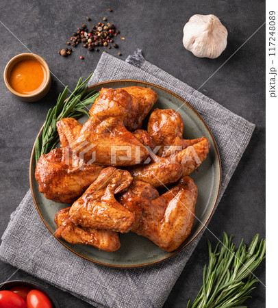Spicy grilled chicken wings with sauce on a plate with tomato and herb on a dark background  117248089