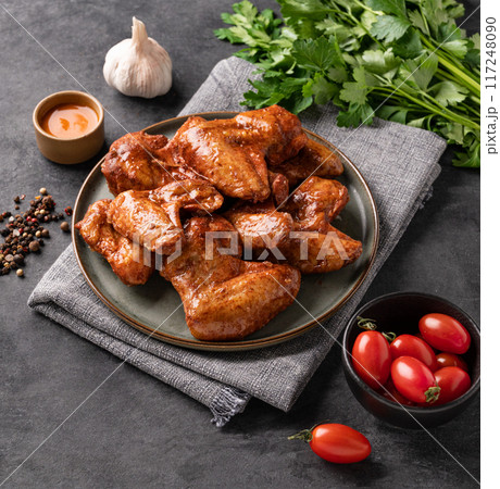 Spicy grilled chicken wings with sauce on a plate with tomato and herb on a dark background  117248090