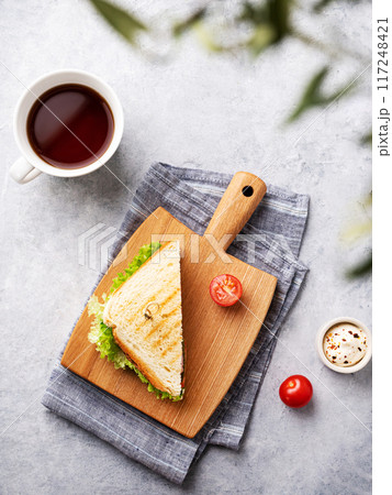 Club sandwich on a wooden board of ham, cheese, tomato and lettuce leaves on a blue background  117248421