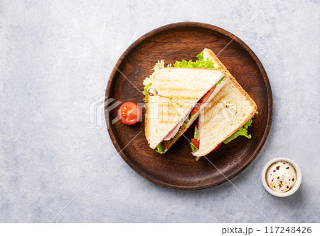 Club sandwich on a wooden plate of ham cheese, cucumber, tomato and lettuce leaves Club sandwich on a wooden plate of ham cheese, cucumber, tomato and lettuce leaves 117248426