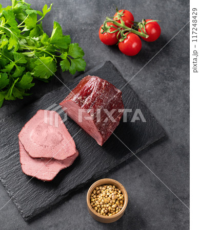 Juicy baked roast beef on a slate board with tomatoes and fresh herbs on a dark background. Juicy baked roast beef on a slate board with tomatoes and fresh herbs on a dark background. 117248429