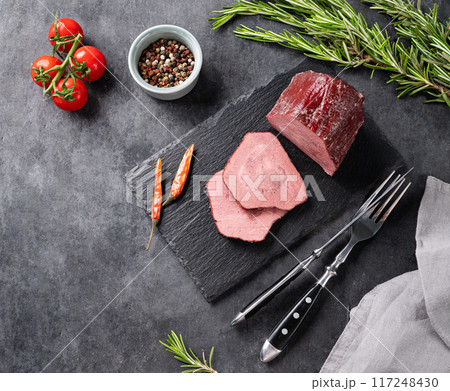 Juicy baked roast beef on a slate board with tomatoes, pepper and fresh herbs on a dark  background. 117248430