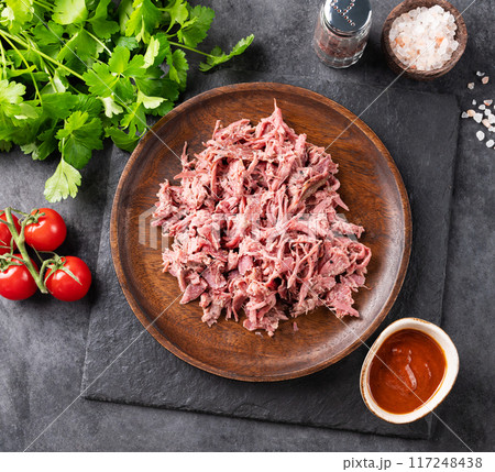 Traditional barbecue torn beef or lamb meat on wooden plate with bbq sauce, fresh tomatoes and herbs 117248438