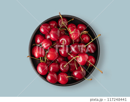 Juicy cherries in a black bowl on a blue background. Top view and copy space 117248441