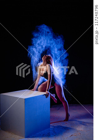 Young woman posing with blue particles in the air Young woman posing with blue particles in the air 117248796