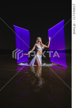 Young slim girl posing in water with abstract purple light effect Young slim girl posing in water with abstract purple light effect 117248817