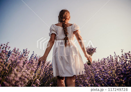 Lavender field girl. Back view happy girl in white dress with a scythe runs through a lilac field of lavender. Aromatherapy travel Lavender field girl. Back view happy girl in white dress with a scythe runs through a lilac field of lavender. Aromatherapy travel 117249728