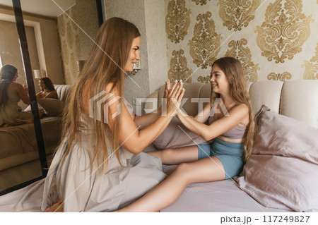 mom and daughter are playing together on a bed. The woman is holding the child's hand and they are both smiling. Scene is happy and playful. 117249827
