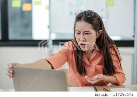 A woman in an orange shirt is looking at a laptop computer A woman in an orange shirt is looking at a laptop computer 117250572