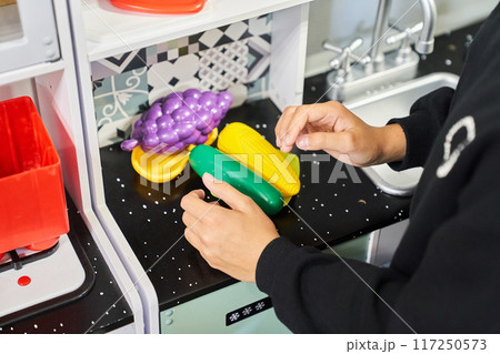A girl cooks in a toy kitchen. Plastic toys for small children. Children play and cook at home or in kindergarten. Kids play with a stove, dishes, sink, vegetables. High quality photo A girl cooks in a toy kitchen. Plastic toys for small children. Children play and cook at home or in kindergarten. Kids play with a stove, dishes, sink, vegetables. High quality photo 117250573