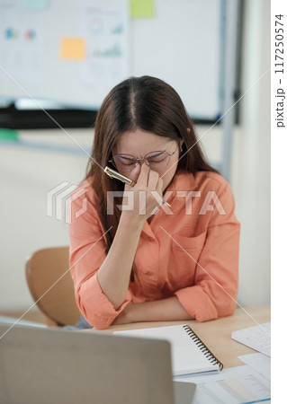 A woman is sitting at a desk with a pen and a notebook 117250574