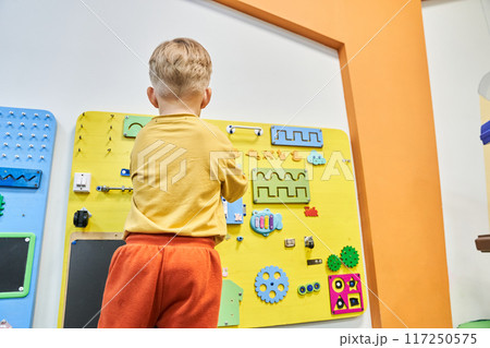 A child is playing a wooden maze on the wall. Educational logic toys for kids. An unrecognizable child with his back to the camera with a copy space. High quality photo 117250575
