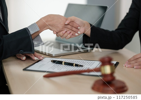 Two people shaking hands in front of a laptop and a judge's gavel Two people shaking hands in front of a laptop and a judge's gavel 117250585
