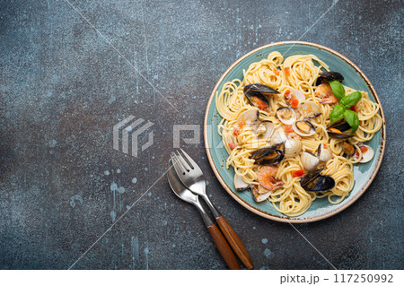 Italian seafood pasta spaghetti with mussels, shrimps, clams in tomato sauce with green basil on plate on rustic blue concrete background top view. Mediterranean cuisine, space for text 117250992