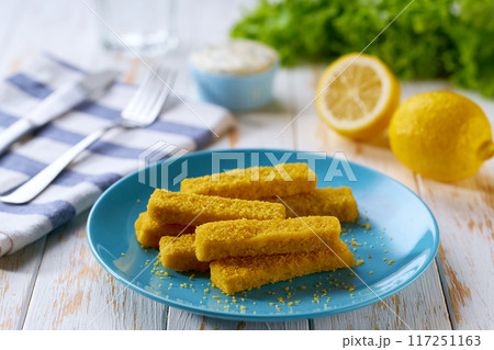 Crispy breaded deep fried fish fingers with lemon and tartar sauce on wooden table. 117251163