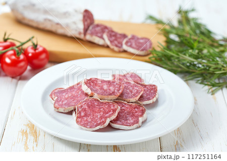 traditional Spanish salami fuet sausage or dry sausage cut in slices on a white ceramic plate, isolated on a kitchen table. traditional Spanish salami fuet sausage or dry sausage cut in slices on a white ceramic plate, isolated on a kitchen table. 117251164