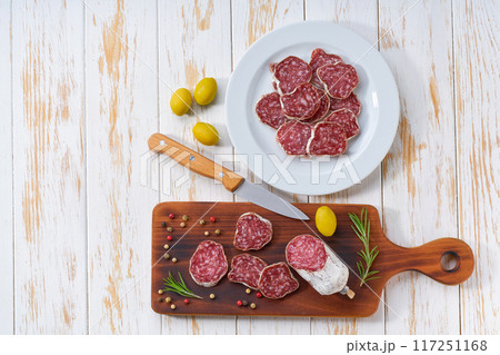 traditional Spanish salami fuet sausage or dry sausage cut in slices on a white ceramic plate, on a kitchen table, top view. traditional Spanish salami fuet sausage or dry sausage cut in slices on a white ceramic plate, on a kitchen table, top view. 117251168