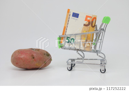 Raw potato tuber and a toy grocery cart on a white background. World food crisis. Raw potato tuber and a toy grocery cart on a white background. World food crisis. 117252222
