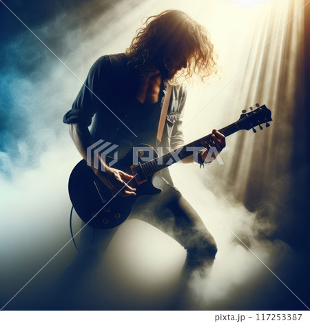 Rock guitarist playing guitar in a haze against the background of incident rays of light. 117253387