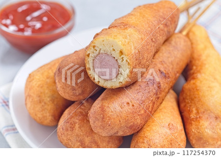 Corn dogs on white plate, served with ketchup, horizontal closeup Corn dogs on white plate, served with ketchup, horizontal closeup 117254370