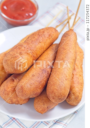 Stack of corn dogs on white plate, served with ketchup, vertical closeup 117254372