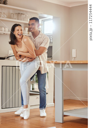 Interracial, fun and carefree couple hugging, bonding and laughing while relaxing together at home. Caring, loving and relaxed boyfriend and girlfriend enjoying romantic holiday and embracing 117254444