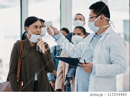 Travel medical healthcare worker testing covid temperature at airport using infrared thermometer. Professional doctor doing a coronavirus check up on a woman at an office entrance Travel medical healthcare worker testing covid temperature at airport using infrared thermometer. Professional doctor doing a coronavirus check up on a woman at an office entrance 117254493