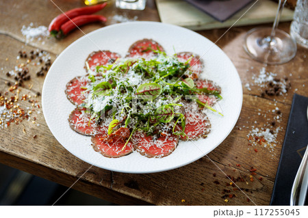 Beef carpaccio. Borettane onion, sun-dried tomato, truffle dressing, arugula salad, parmesan cheese. Italian traditional antipasti snacks served for lunch with wine in modern gourmet restaurant Beef carpaccio. Borettane onion, sun-dried tomato, truffle dressing, arugula salad, parmesan cheese. Italian traditional antipasti snacks served for lunch with wine in modern gourmet restaurant 117255045