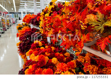 A store aisle filled with vibrant artificial autumn flowers and decorations 117255331