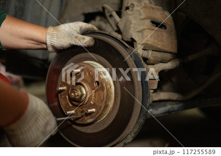In the workshop, a male mechanic is changing the brake discs on a car. A man unscrews the bolts holding the brake disc with a screwdriver. concept of repairing a brake disc on a car. In the workshop, a male mechanic is changing the brake discs on a car. A man unscrews the bolts holding the brake disc with a screwdriver. concept of repairing a brake disc on a car. 117255589
