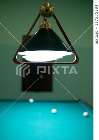 A billiard triangle hangs on a lamp above the table. After placing the balls in the center of the table, the billiard pyramid was hung on the lamp above the table. Billiard pyramid, triangle concept. A billiard triangle hangs on a lamp above the table. After placing the balls in the center of the table, the billiard pyramid was hung on the lamp above the table. Billiard pyramid, triangle concept. 117255593