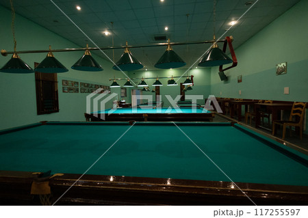 Empty billiard room with green tables illuminated by lamps. Beautiful game room for billiards without people. Many pool tables stand empty, waiting for players. 117255597